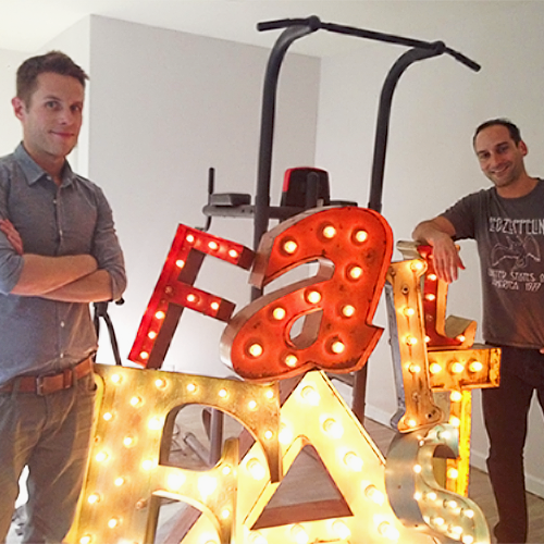 Two people holding illuminated EK marquee letters, a 2015 company photo 