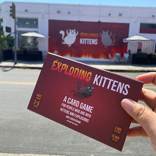 Hand holding the Exploding Kittens card game box outdoors 